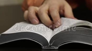 桌子上放着一本公开的圣经。 这个人迅速翻页寻找想要的<strong>章节</strong>。 找到并肯定地戳到