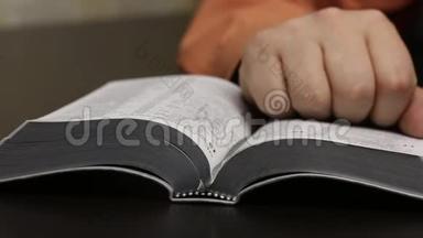 桌子上放着一本公开的圣经。 一个人读它，移动他的手指沿着线条，<strong>翻页</strong>。 撕下书签，关闭