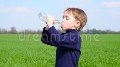 一个小男孩用塑料瓶里的水解渴。 在阳光明媚的日子里，一个孩子在大自然中喝水。