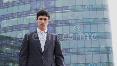 穿着商务套装和领带的白人帅哥站在一栋带有全景窗户的高层建筑的背景下。