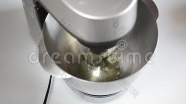 搅拌机在金属碗中搅拌鸡蛋蛋白。 搅拌机把蛋清打成厚厚的泡沫。 鸡蛋用搅拌机搅拌成泡沫状