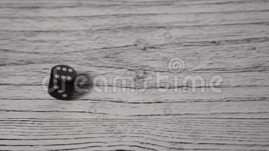 黑色骰子在白色纹理的木制旧桌子上滚动和旋转。 上面有数字6的地方