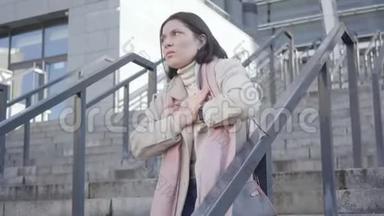 镜头接近悲伤的白种人女商人站在楼梯上，双手放在胸前。 年轻的黑发女人