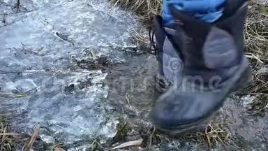 特写镜头`人的双脚穿着高靴踩在冰上，掉进水坑里
