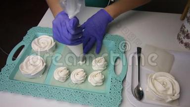 托盘上摆着一个玫瑰形的棉花糖。 一个女人在糕点袋的帮助下形成了一个经典形状的棉花糖