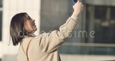 开朗的高加索女人自拍的肖像。 年轻的黑发女士用智能手机在城市大<strong>街拍</strong>照