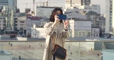 自信的高加索女人在城市街头拍照。 商务女士站在摩天大楼的背景下使用