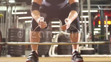 年轻的健美运动员准备在现代健身馆举起沉重的杠铃，手握滑石粉