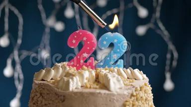 生日蛋糕有22个数字，由较轻的粉红色蜡烛燃烧在蓝色的背景上。 蜡烛被点燃了。 慢动作