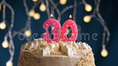 生日蛋糕，蓝色背景上有30个数字的粉红色燃烧蜡烛。 蜡烛吹灭了。 慢速运动和特写镜头