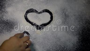 面粉洒在桌子上。 他们用手指在上面画<strong>一颗</strong>心。 情人节。 黑暗的大理石背景。 白色面粉。