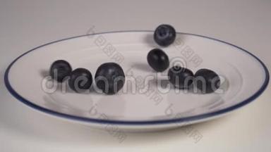 成熟的蓝莓落在白色的盘子上，蓝色的边框