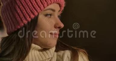 可爱的高加索人女孩冬季帽子和毛衣的特写镜头回望五颜六色的旋转木马。年轻漂亮的女人