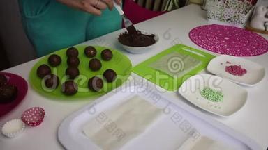 一个女人把海绵蛋糕上的球浸到巧克力里。 做一个土豆蛋糕。 盘子旁边有蛋糕、液体巧克力和