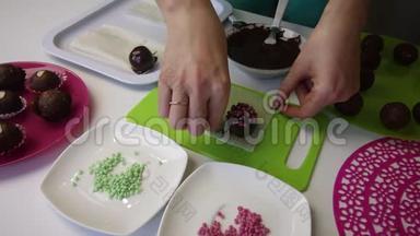 一个女人把巧克力球洒在海绵蛋糕上。 做一个土豆蛋糕。 盘子旁边有蛋糕、液体巧克力和