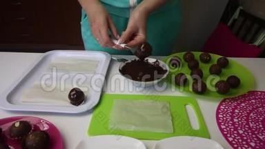 一个女人把海绵蛋糕上的球浸到巧克力里。 掉多余的釉料.. 做一个土豆蛋糕。 盘子旁边是蛋糕