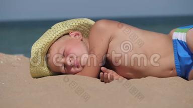 男孩躺在金沙上。 这孩子戴着一顶大<strong>帽檐</strong>的草帽. 孩子睡在海滩上。