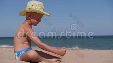 男孩坐在金沙上。 这孩子戴着一顶大<strong>帽</strong>檐的草<strong>帽</strong>. 孩子在<strong>沙滩</strong>上玩