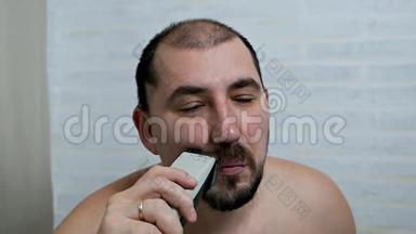 一个男人在家里用电动剃须<strong>刀刮胡子</strong>和<strong>胡子</strong>，在镜子前脱毛。 男人`照顾