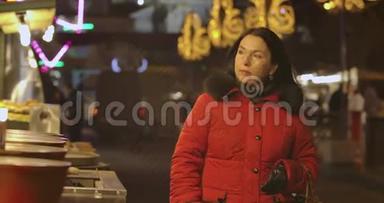 一幅自信的白种人女人穿着红色外套，晚上沿着城市市场走来走去，环顾四周。 积极正面