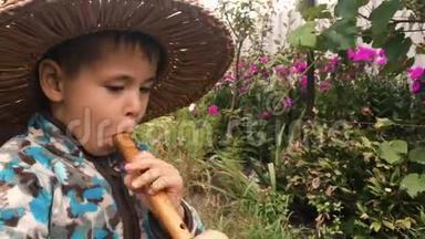 戴草帽的小男孩试图在绿色花园里的木制乐器上演奏。 小可爱的男孩喜欢吹笛子，靠近