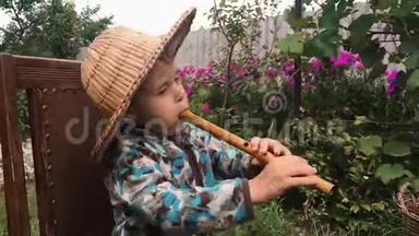 小可爱的白种人孩子戴着草帽在花园里吹着<strong>木笛</strong>。 在vi演奏乐器的可爱的小男孩