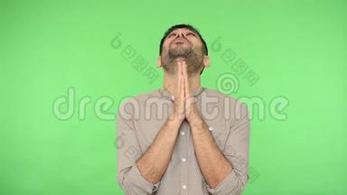 愁眉苦脸的黑发男子在祈祷中紧握双手，用恳求的表情抬起头来。 绿色背景，色度键
