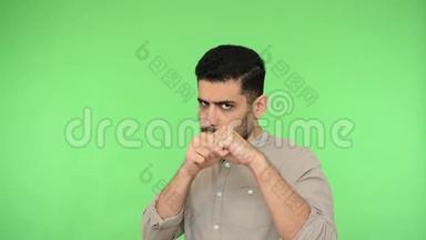 愤怒的黑发男人，穿着衬衫，举起拳头，在镜头前冲着空气。 绿色背景，色度键