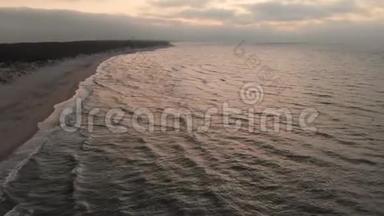 空中观看无人机镜头低飞行在一个废弃的海滩上日落。 带着滚滚海浪和夕阳的沙岸
