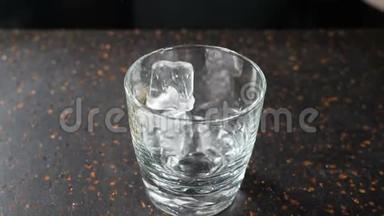 在黑暗的酒吧柜台上，用杯中的冰块倒入空的透明玻璃杯中，用于威士忌、白兰地或波旁酒，缓慢