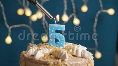 生日蛋糕与5号燃烧蜡烛，由<strong>打火</strong>机在蓝色的背景。 蜡烛被点燃了。 慢速运动和特写镜头