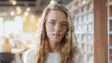 一个戴眼镜的聪明女孩在大学<strong>图书馆</strong>的背景下看着摄像机的照片。聪明的少年