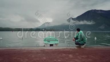 穿着薄荷雨衣的人坐在山上的一个湖上，靠近一艘颜色相同的停泊船。 雨天。 安纳西湖