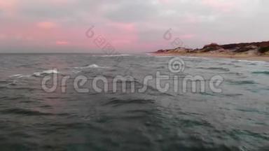 空中观看无人机镜头低飞行在一个废弃的海滩上日落。 带着滚滚波浪和粉红云彩的沙滩