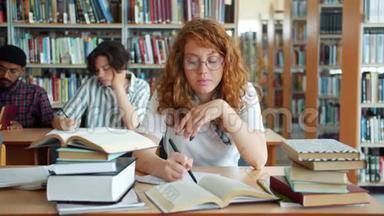疲倦的红头发女孩在图书馆学习，然后睡在桌子上，在室内放松