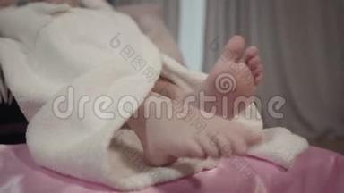 穿着<strong>白色浴袍</strong>躺在粉红色床上的白种人小女孩的特写双脚。 洗澡后的孩子在她的房间里休息