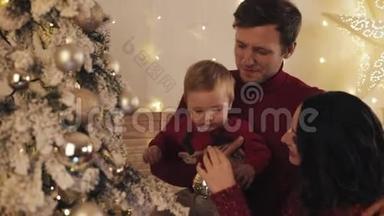 爸爸妈妈和宝宝幸福的<strong>一家</strong>人站在家中的圣诞树旁，爸爸<strong>抱着</strong>小男孩亲吻他