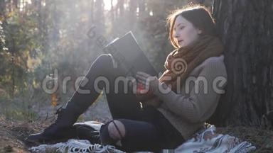 快<strong>乐</strong>的<strong>怀旧</strong>女人旅行者在秋天的森林里看书和看日落。 年轻的模特女游客坐在秋天