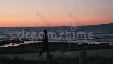 日落时分，孤独的年轻女子沿着地中海海滨散步。 穿着保暖衣服的漂亮女人在沙滩漫步