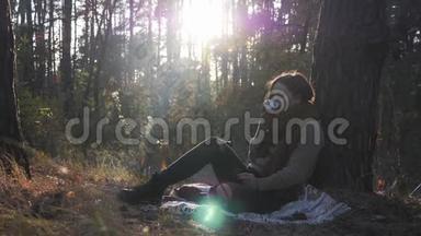 幸福迷人的女人坐在外面的格子布上喝咖啡。 美丽的黑发女人，穿着舒适的毛衣和温暖的围巾怀旧