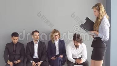 一群年轻人无聊地坐在走廊办公室的椅子上等待面试。 公司招聘