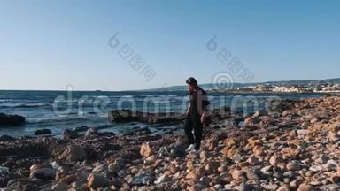 孤独忧郁的年轻女子走在空荡荡的鹅卵石海滩上。 年轻女子沿着污染的海滩散步。 伤心的女人走在人群中