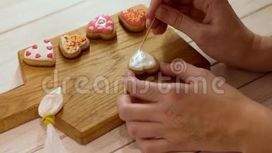用糖霜装饰姜饼的过程。 女人的双手为情人节装饰心形饼干