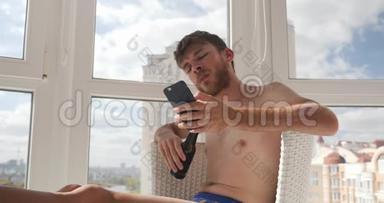 醉酒的年轻人穿着内裤坐在家里，在手机上输入信息，喝酒