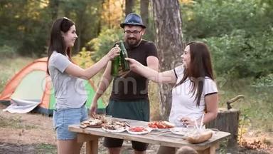 休闲和人的概念-快乐的朋友在森林里举杯，喝酒，在日落时带帐篷的<strong>夏日派对</strong>。