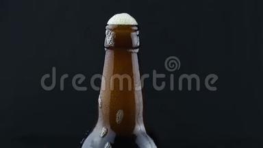啤酒泡沫从一个雾状的瓶子里流下来。 泡沫顺着一瓶深色啤酒流下来.. 深色背景下的一瓶啤酒。