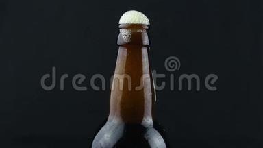 啤酒泡沫从一个雾状的瓶子里流下来。 泡沫顺着一瓶深色啤酒流下来.. 深色背景下的一瓶啤酒。