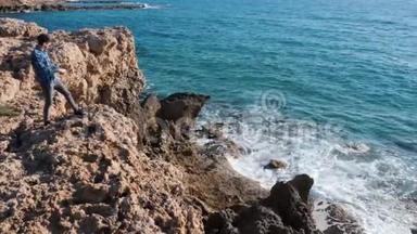 年轻人站在石头上，把石头扔进水里。 站在悬崖边上的白人男孩把石头扔进海里。 曼斯坦