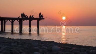 渔夫的<strong>剪影</strong>与钓竿在海上日落坐在码头上。慢动作。
