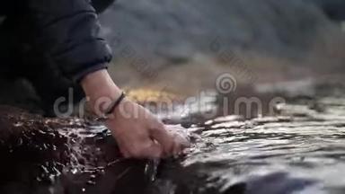 双手特写。 一个徒步旅行者把手伸进一条冰冷的河里。 特写镜头。